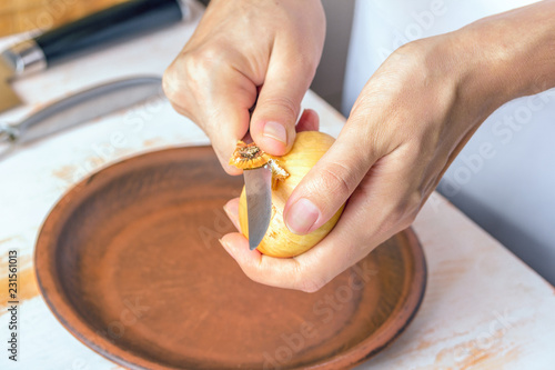 Onion and knife in female hands close-up, cleaning onions. Cooking process. The concept of homemade food.