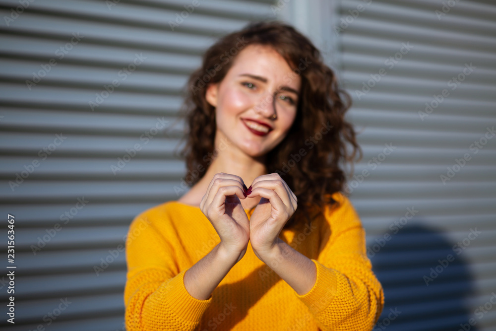 © vpavlyuk - Lifestyle shot: expressive brunette girl in yellow knitted sweater holding heart shaped hands, posing near shutters