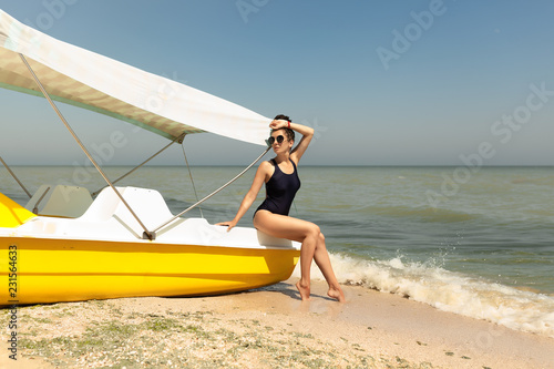 Pretty young woman wearing black swimsuit and sunglasses posing on the catamaran photo