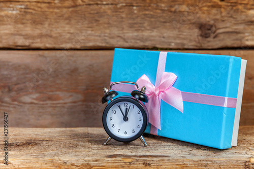 Alarm clock and gift box wrapped blue paper. Christmas or new year decorated gift on old shabby rustic wooden background. Christmas birthday valentine Time for celebration present romantic concept photo