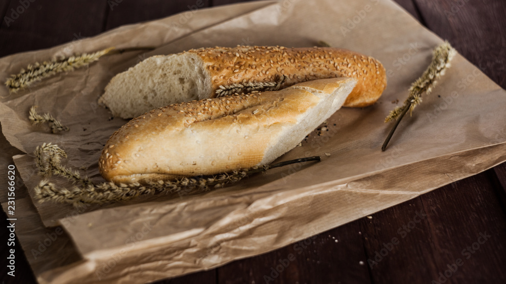 French baguettes with sesame seed on a paper bag lie on a wooden table. French baguettes with sesame seed on a paper bag lie on a wooden table.