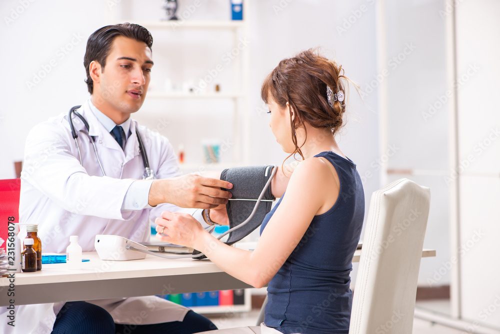 Fototapeta premium Young doctor checking woman's blood pressure