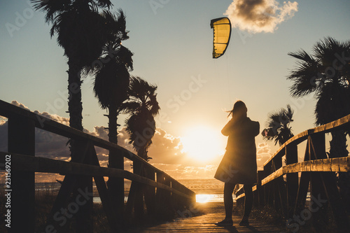 Woman taking a picture of a sunset in Tarifa, Spain. Kitesurfing kite in the background.