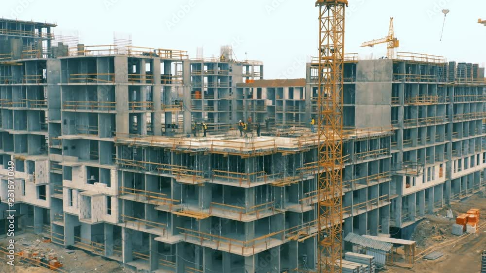 The corner of a big construction site with a houses in a course of building with a lot of workers in colorful helmets. Aerial rotating shot 
