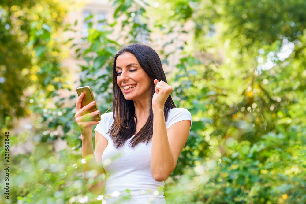 A cheerful woman in a Park receiving good news on her Smartphone A cheerful woman in a Park receiving good news on her Smartphone