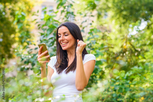 A cheerful woman in a Park receiving good news on her Smartphone