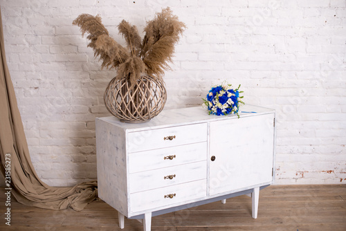 White wood bedside table, dresser in bedroom. bridal bouquet on the nightstand vase with flowers. interior. Series of furniture loft style. Modern designer.