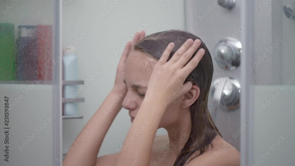 Smiling young girl bathing under a shower at home. Beautiful teen