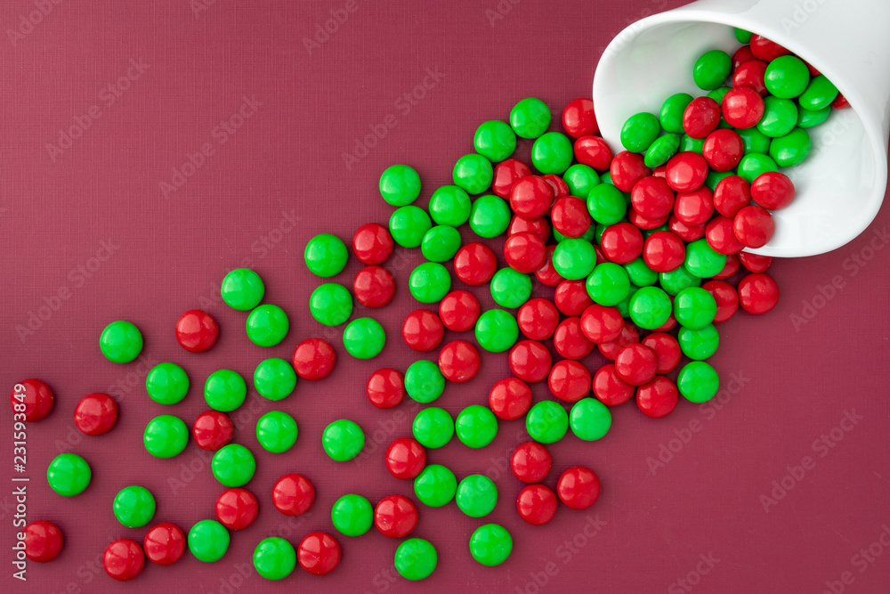 Red and green Christmas candy spilling out of a white bowl onto a red background
Red and green Christmas candy spilling out of a white bowl onto a red background