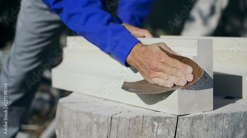 master is polishing a wooden product with an emery cloth by his hands on a stump in the street in the afternoon.