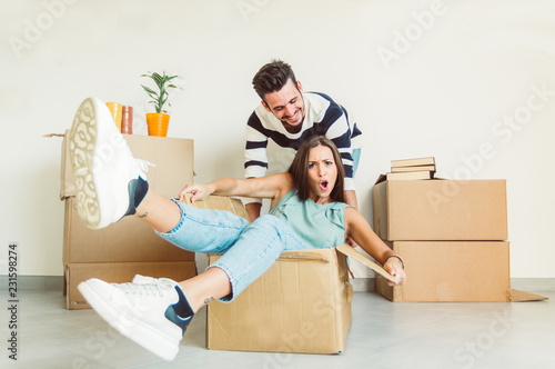 Happy couple having fun moving in the new house playing riding cardboards photo