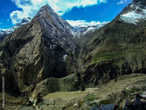 The view of snowy mountains and peak with blue sky, clouds and river