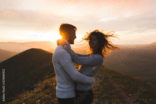 Happy couple hugging and kissing at sunset witn amazing mountain view. Warm evening sun light