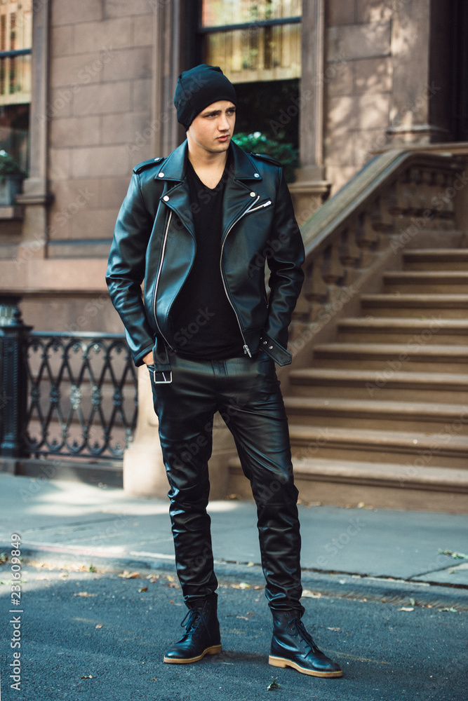 Hipster man wearing black style leather outfit with hat, pants, jacket and  shoes standing on city street Stock Photo