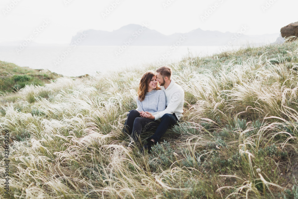 Happy young loving couple sitting in feather grass meadow, laughing and hugging, casual style sweater and jeans Happy young loving couple sitting in feather grass meadow, laughing and hugging, casual style sweater and jeans