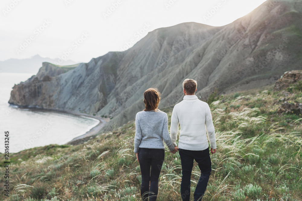 Young couple walking on nordic sea coast with mountain view in spring, casual style clothing sweaters and jeans