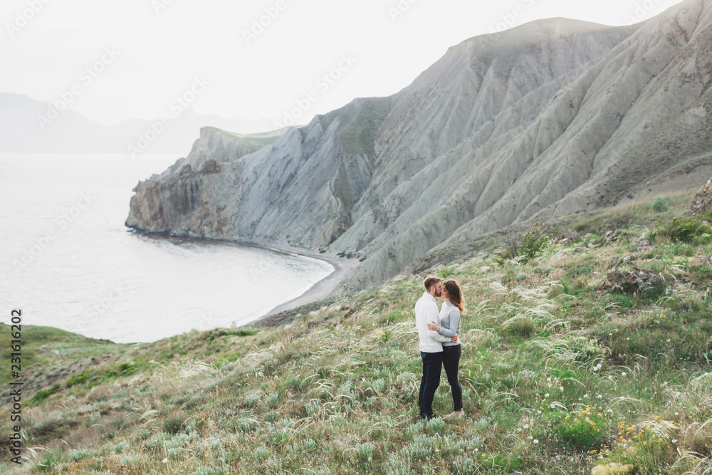 Young couple walking on nordic sea coast with mountain view in spring, casual style clothing sweaters and jeans Young couple walking on nordic sea coast with mountain view in spring, casual style clothing sweaters and jeans