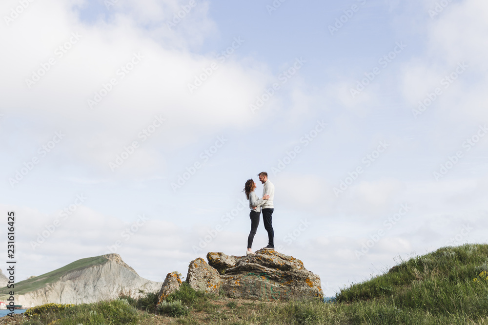 Obraz premium Young couple walking on nordic sea coast with mountain view in spring, casual style clothing sweaters and jeans