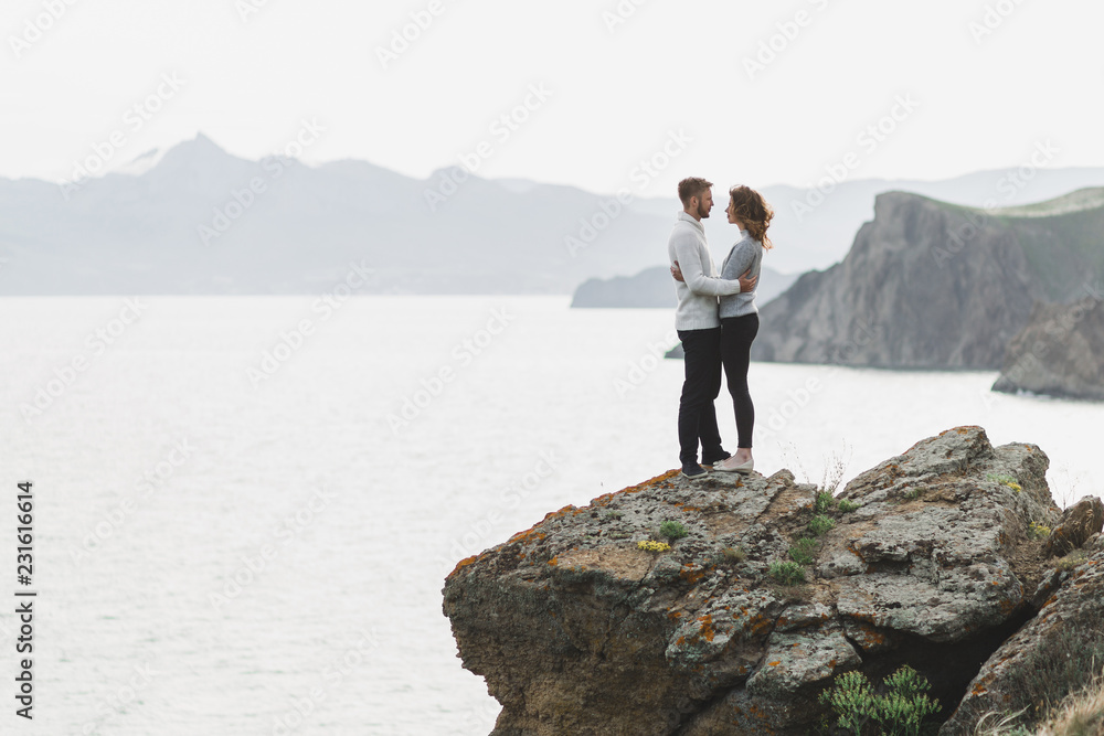Young couple walking on nordic sea coast with mountain view in spring, casual style clothing sweaters and jeans Young couple walking on nordic sea coast with mountain view in spring, casual style clothing sweaters and jeans