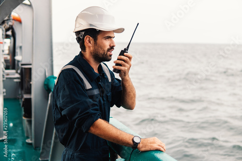 Marine Deck Officer or Chief mate on deck of vessel or ship . He holds VHF walkie-talkie radio in hands. Ship communication photo