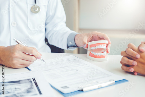Dentist talking to smiling male patient and showing denture in dental office