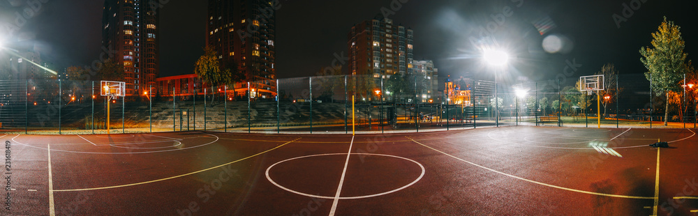 Illuminated basketball playground with red pavement, modern new basketball net and lens flares on background. 
