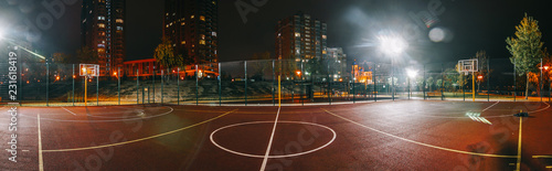 Oświetlony plac zabaw do koszykówki z czerwonym chodnikiem, nowoczesną siatką do koszykówki i flarami obiektywu w tle