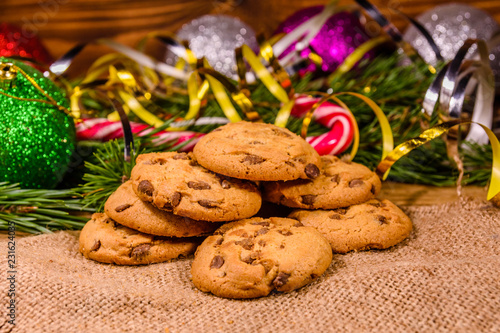 Pile of the chocolate chip cookies on sackcloth in front of christmas decorations