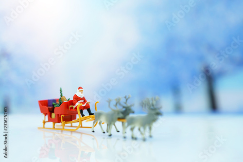 Miniature people: Santa Claus sitting Reindeer Sleigh with greeting or postal card and christmas tree. Christmas and Happy New Year concept. © Rattana.R