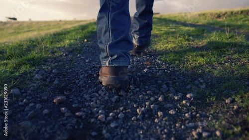 Camera tracking behind man in blue jeans and boots walking down a lonely track at sunrise.