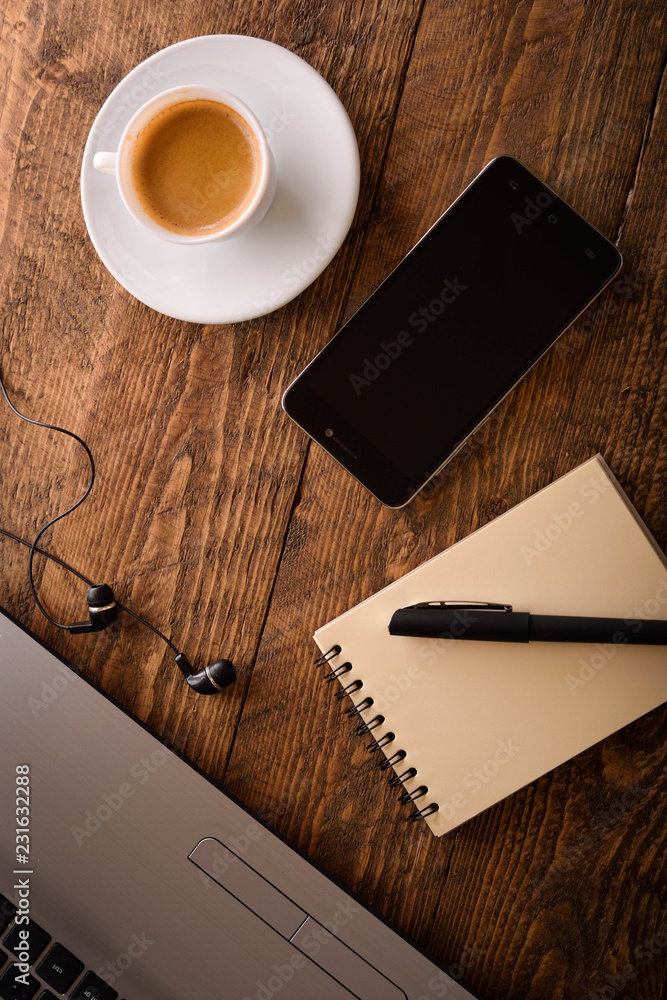 Laptop (notebook) mobile phone (smartphone) and notepad with pen on old wooden table. Work place modern.Cup of coffee Laptop (notebook) mobile phone (smartphone) and notepad with pen on old wooden table. Work place modern.Cup of coffee