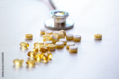 The medicines and fish oil tablets on the white surface with stethocope in the natural light photo