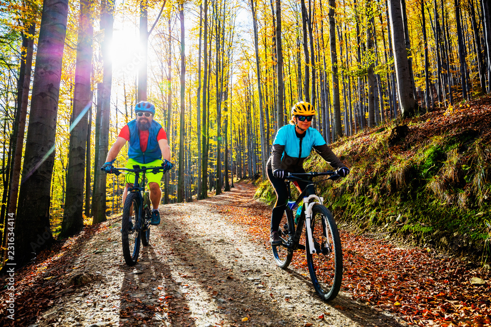 Obraz premium Cycling woman and man at Beskidy mountains autumn forest landscape. Couple riding MTB enduro track. Outdoor sport activity.