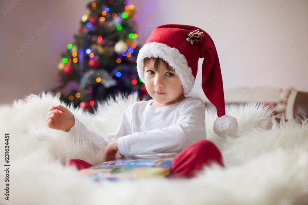 Cute adorable boy reading a book in front of the christmas tree Cute adorable boy reading a book in front of the christmas tree