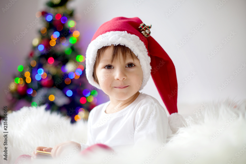 Cute adorable boy reading a book in front of the christmas tree Cute adorable boy reading a book in front of the christmas tree