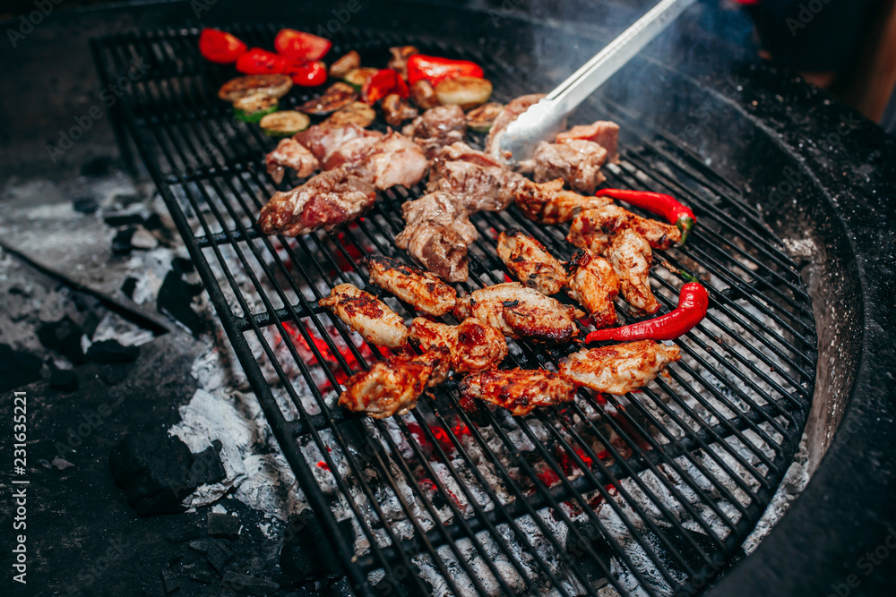 Grilled meat and vegetables in barbecue with flames and coals.