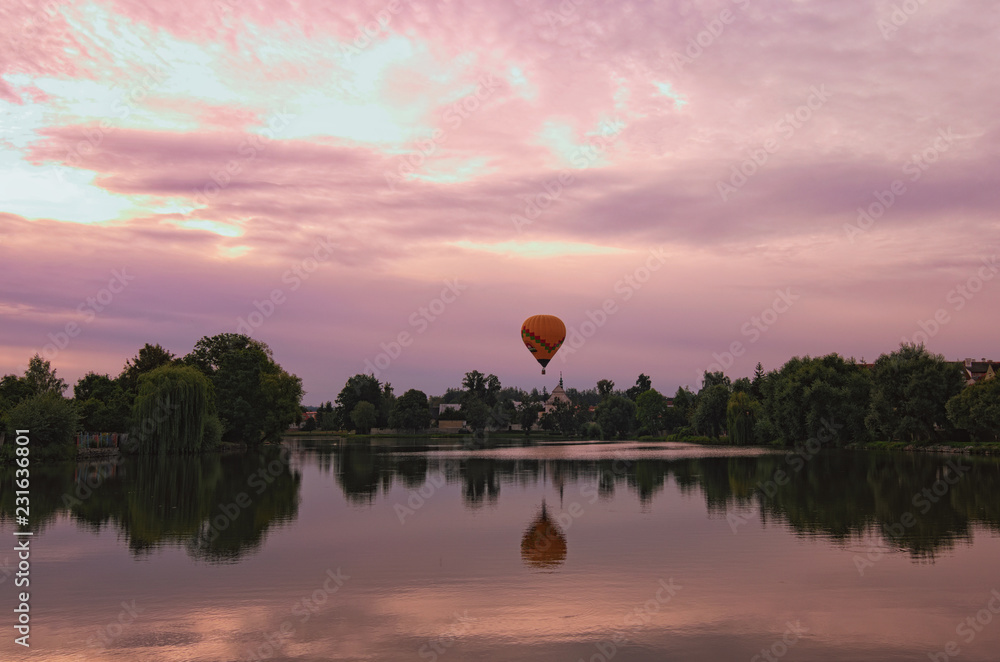 Obraz premium Picturesque view of medieval Telc during magic sunrise. One hot air balloon flies over the houses and reflected on smooth lake water. Summer landscape. Telc, Southern Moravia, Czech Republic