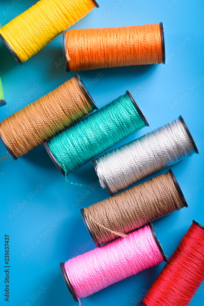 Colored thread coils on blue background, sewing, place for text Colored thread coils on blue background, sewing, place for text