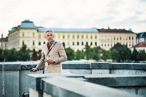 Photography Mature businessman with suitcase standing on a bridge in Prague city