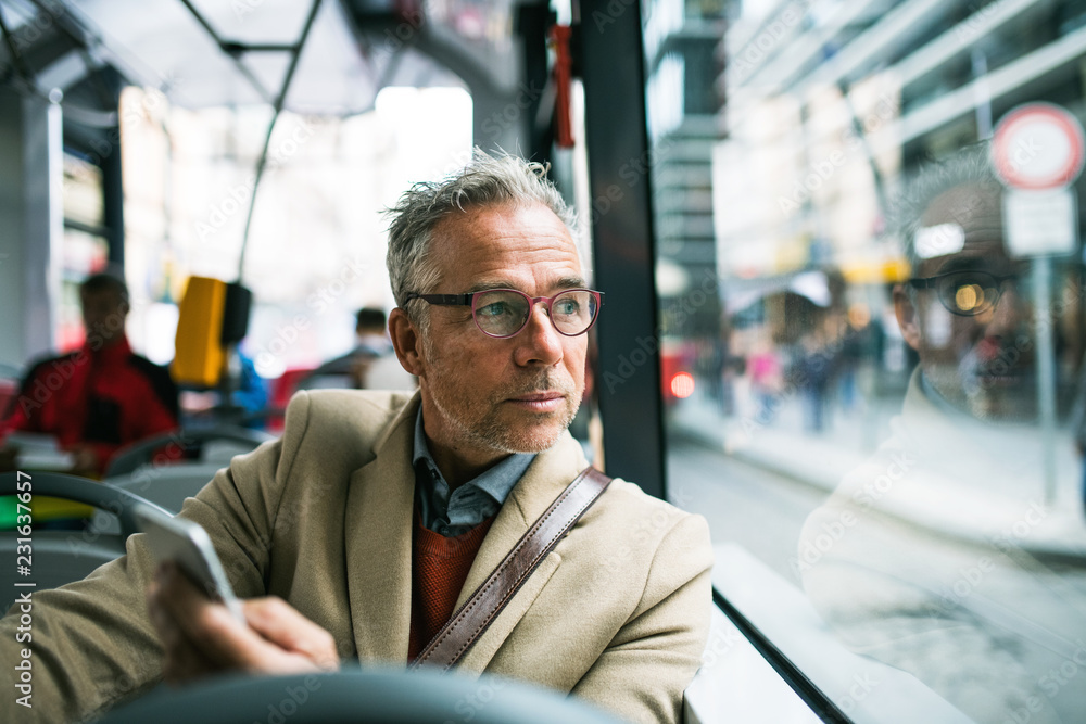 Mature businessman with smartphone travelling by bus in city. Mature businessman with smartphone travelling by bus in city.