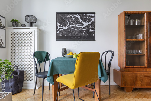 Retro china cabinet in eclectic living room interior with yellow chair and map on the wall, real photo