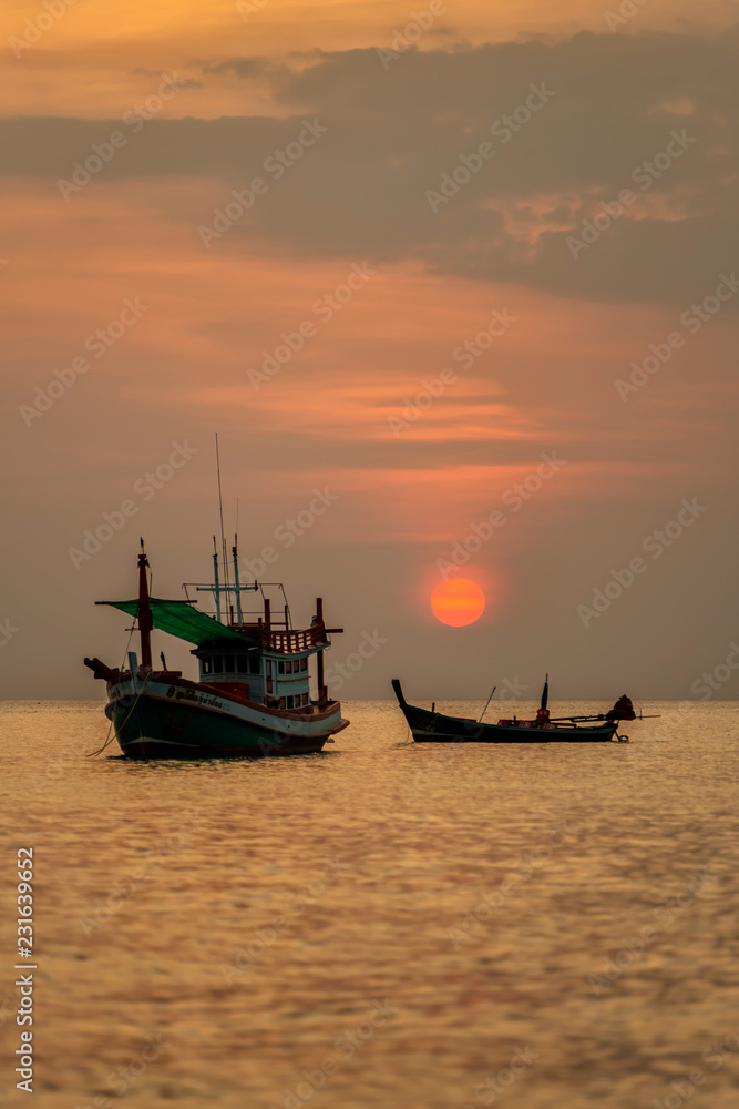 Boat sailing along its journey against a vivid colorful sunset in formation against an orange and yellow color filled sky sunset fantasy with a silhouette in Thailand.
