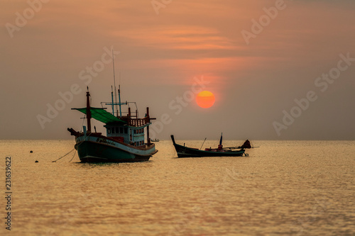 Boat sailing along its journey against a vivid colorful sunset in formation against an orange and yellow color filled sky sunset fantasy with a silhouette in Thailand.