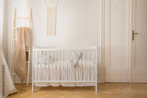 Scandinavian nursery with white wooden crib and macrame on the wall in tenement house, real photo with copy space photo