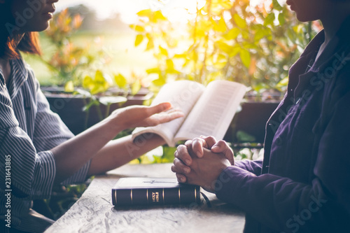 Asian girls are reading the sacred scriptures by pointing to the text of the book. And share the gospel and to explain the meaning of the Bible to her friend understand. Amid the meadows and greenery