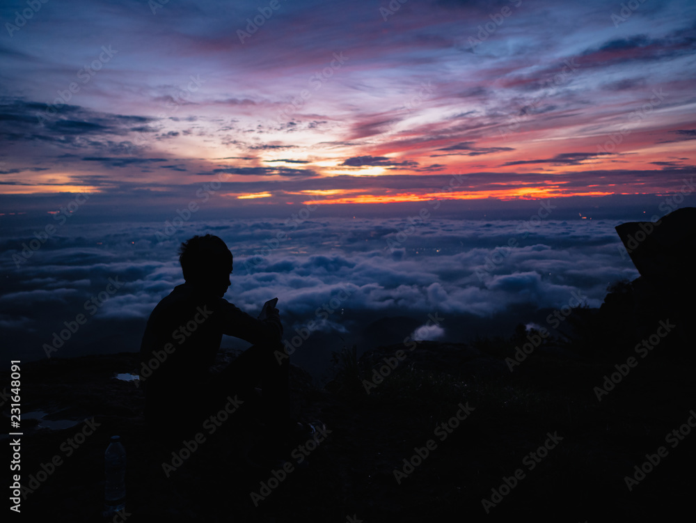 Silhouette People Sit on the cliff with beautiful sunrise sky on on Khao Luang mountain in Ramkhamhaeng National Park,Sukhothai province Thailand