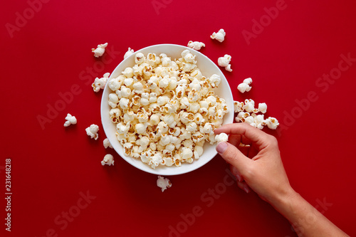 Hand picking popcorn in white bowl against red background.