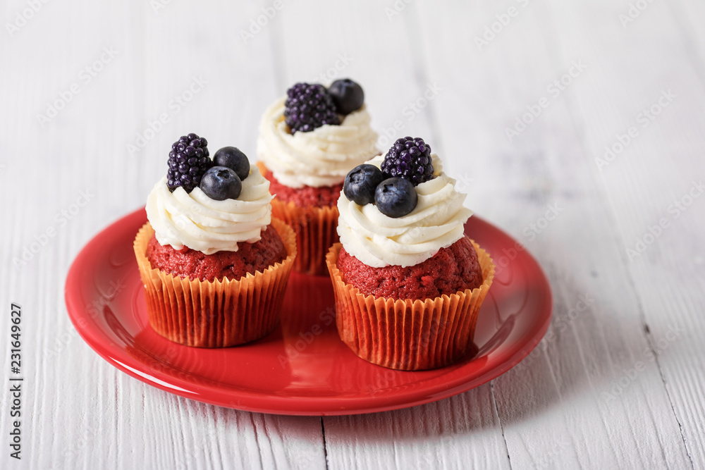 Tasty red velvet cupcakes with blueberry and blackberry on wooden table.