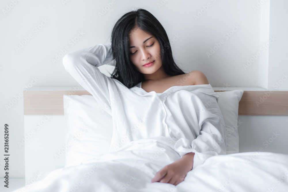 Beautiful young pretty Asian woman wake up and make happy smile with white shirt at the white bed in the morning. Beautiful young pretty Asian woman wake up and make happy smile with white shirt at the white bed in the morning.