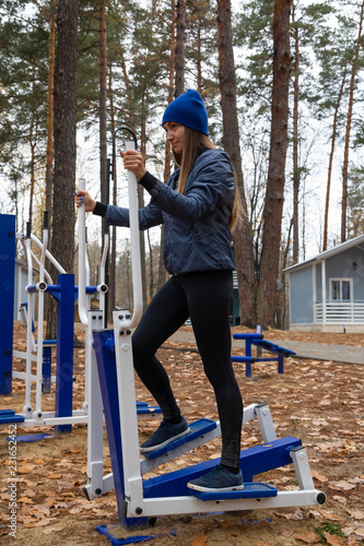A young women does exercises on a sports simulator in nature. Outdoor.